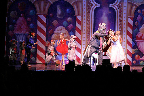 A colorful stage performance featuring dancers in costumes, with a whimsical backdrop of sweets and treats.