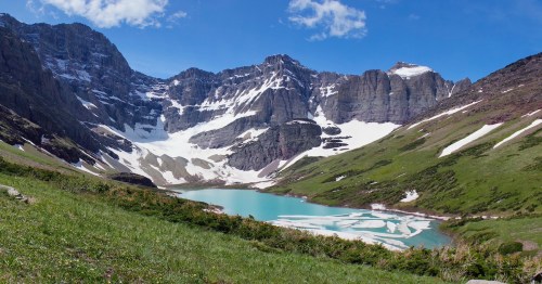 A serene mountain landscape featuring a turquoise lake surrounded by snow-capped peaks and lush green hills.