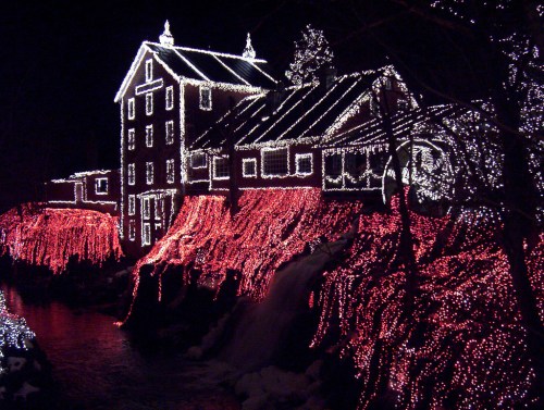 A beautifully lit house and landscape adorned with colorful holiday lights at night, reflecting in the water below.