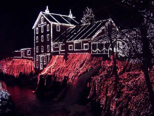 A beautifully lit house and landscape adorned with colorful holiday lights at night, reflecting in the water below.