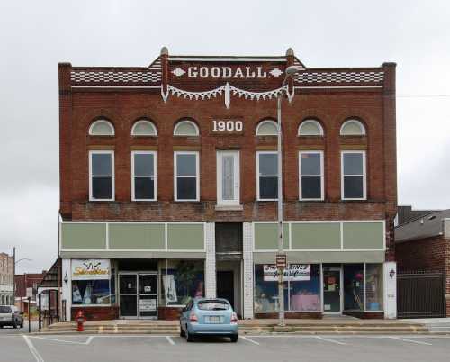 Historic brick building with "Goodall 1900" sign, featuring storefronts and decorative elements on the facade.