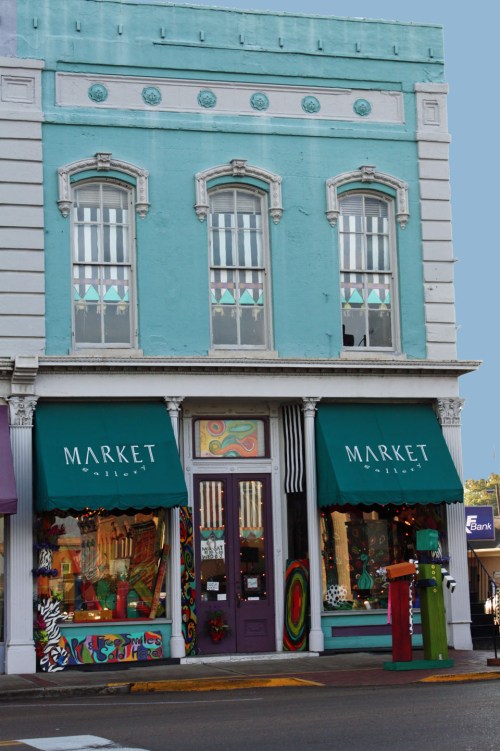 A colorful storefront with "MARKET" signage, featuring vibrant window displays and a turquoise facade.