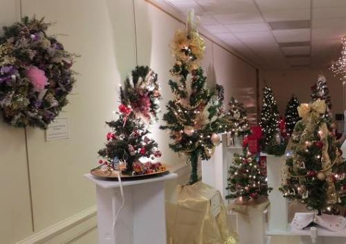 A festive display of decorated Christmas trees and a wreath, showcasing holiday decorations in a bright room.