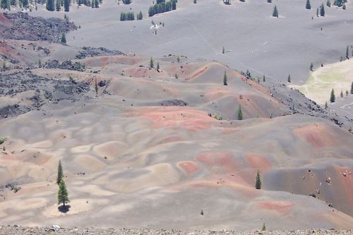 Aerial view of colorful, textured volcanic landscape with scattered trees and gray terrain.