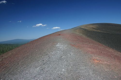A rocky, sloped landscape with a clear blue sky, showcasing a mix of red and gray terrain.