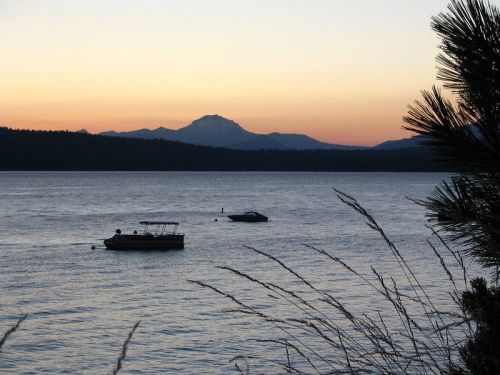 A serene lake at sunset with two boats and a distant mountain silhouette against a colorful sky.