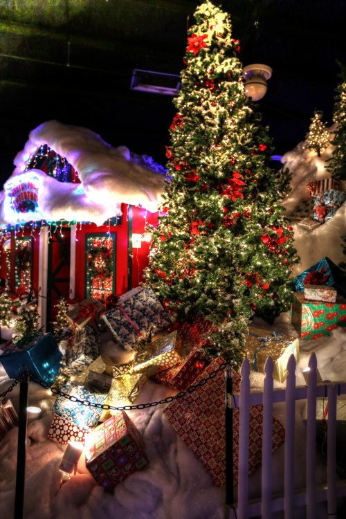 A festive scene featuring a decorated Christmas tree, colorful presents, and a snowy backdrop with twinkling lights.