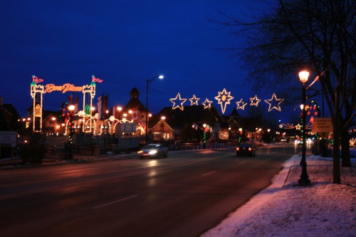 A festive street scene at dusk, adorned with colorful holiday lights and decorations, creating a cheerful atmosphere.