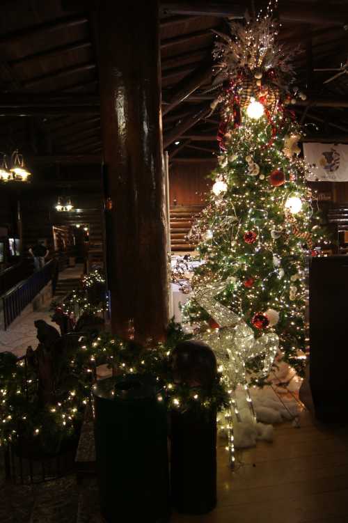 A beautifully decorated Christmas tree with lights and ornaments in a rustic lodge setting.