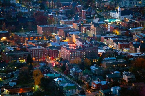 Aerial view of a small town at dusk, featuring historic buildings and a hotel with a glowing sign.