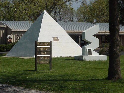 A white pyramid and a modern sculpture beside a sign reading "World's Largest Time Capsule" in a grassy area.