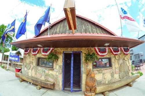 A rustic stone building with a red roof, decorated with flags and bunting, featuring an "Open" sign at the entrance.