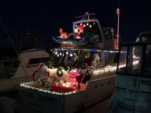 A decorated boat adorned with colorful Christmas lights, featuring a snowman, reindeer, and festive trees.