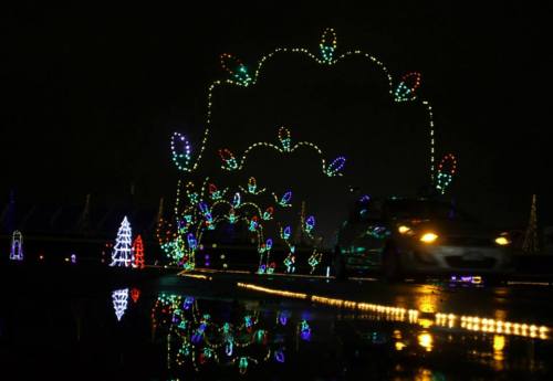 Colorful holiday lights create an arch over a wet road, reflecting the festive decorations at night.