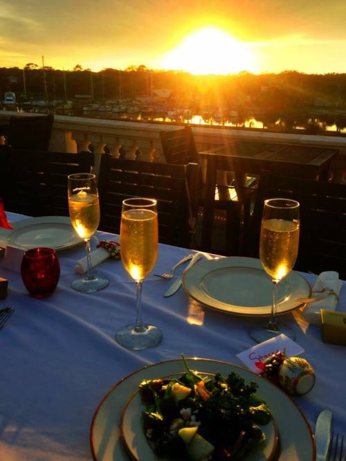 A sunset view from a dining table with champagne glasses and a salad, overlooking a marina.