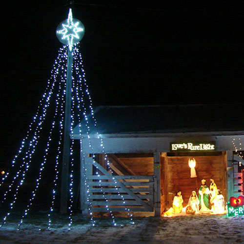 A decorated barn at night with a star on top, surrounded by string lights and a nativity scene.
