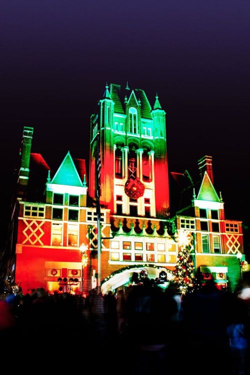 A festive building illuminated with red and green lights, surrounded by a crowd during a holiday celebration.