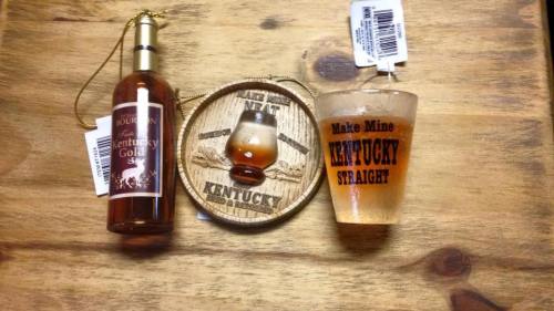 A bottle of Kentucky Gold, a wooden coaster, and a shot glass with "Make Mine Kentucky Straight" on a wooden table.