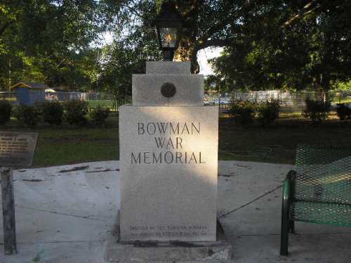 A stone monument labeled "Bowman War Memorial" with a lantern on top, surrounded by greenery and benches.