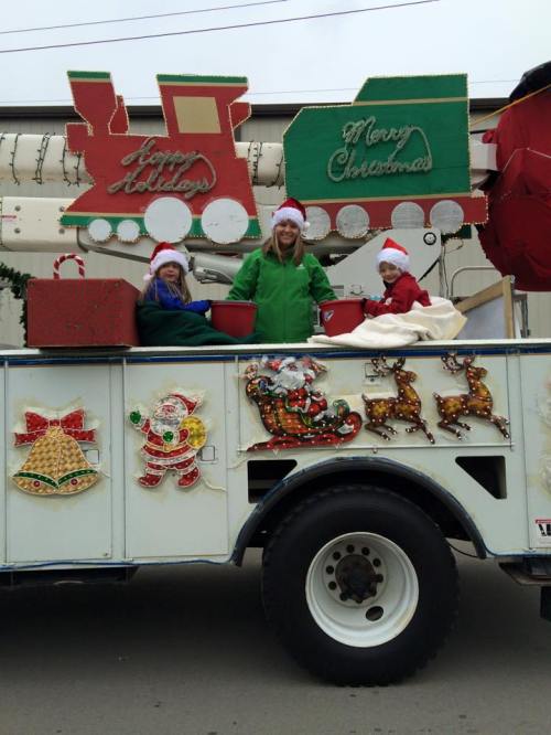 Three children wearing Santa hats sit on a decorated float with holiday decorations, celebrating Christmas.