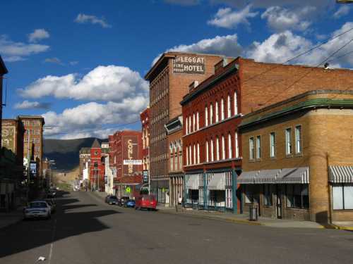 Historic buildings line a quiet street under a blue sky with fluffy clouds, showcasing a small town atmosphere.