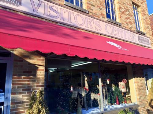 A brick building with a red awning labeled "Visitor's Center," decorated for the holidays with trees and lights.