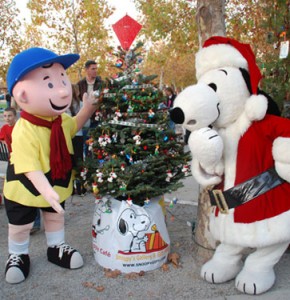 A cartoon character in a yellow shirt and a Santa-clad dog stand beside a decorated Christmas tree.