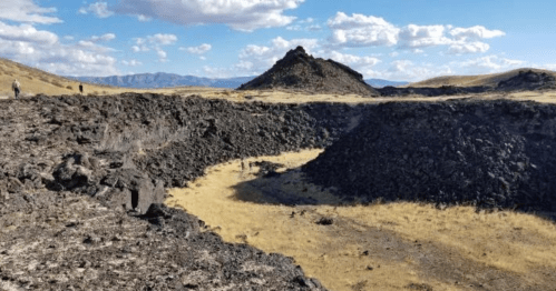 A rocky landscape with volcanic formations and a grassy area under a blue sky with scattered clouds.