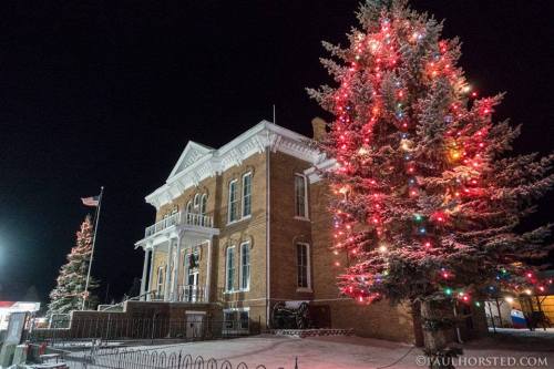 Historic building adorned with festive lights, next to a brightly lit Christmas tree, creating a cheerful winter scene.