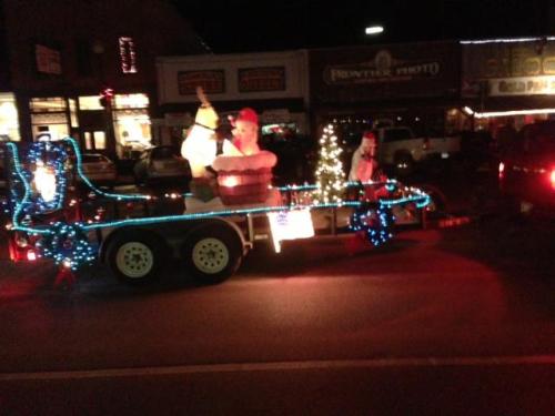 A festive trailer decorated with lights, featuring a snowman, Santa, and a small Christmas tree.