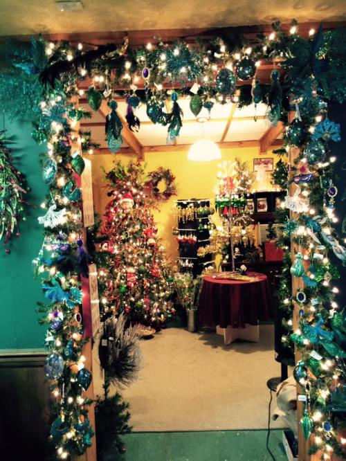 A festive doorway adorned with lights and greenery, leading to a room filled with Christmas trees and decorations.