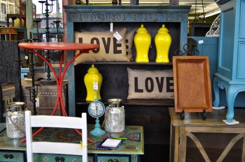 A display of colorful home decor items, including yellow jars, love-themed pillows, and various furniture pieces.