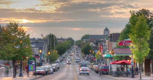 A scenic street view at sunset, lined with trees, shops, and parked cars, creating a vibrant urban atmosphere.