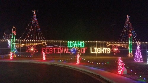 Colorful holiday lights display spelling "Idaho Festival of Lights" with festive decorations and trees at night.