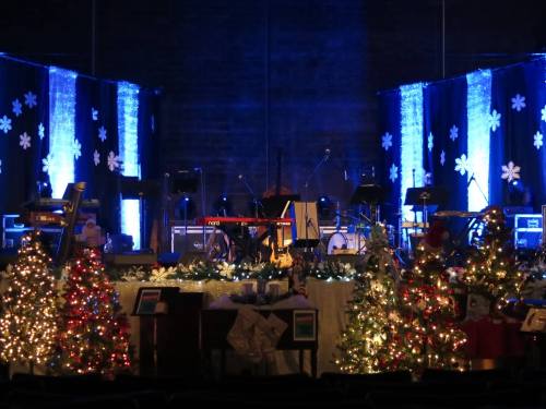 A stage decorated for Christmas with blue lights, snowflakes, and decorated trees on either side.