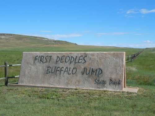 Sign for First Peoples Buffalo Jump State Park, set against a grassy landscape with rolling hills in the background.