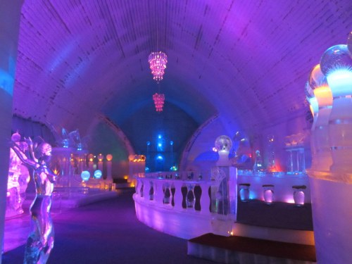 A vibrant, illuminated ice bar with colorful lights, ice sculptures, and a unique architectural design.