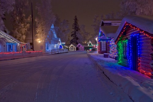 A snowy street lined with colorful, illuminated houses decorated for the winter season at night.