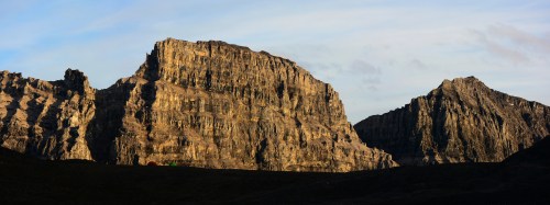 A panoramic view of rugged mountains with dramatic cliffs and a clear sky in the background.