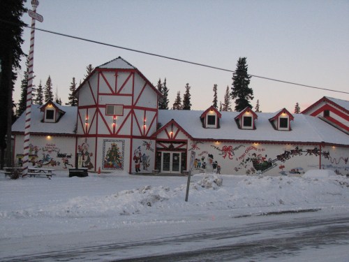 A festive building decorated with holiday murals, surrounded by snow and pine trees, under a clear sky.