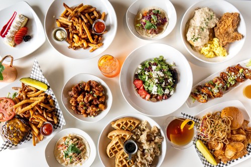 A variety of delicious dishes including fries, salads, chicken, waffles, and drinks arranged on a table.