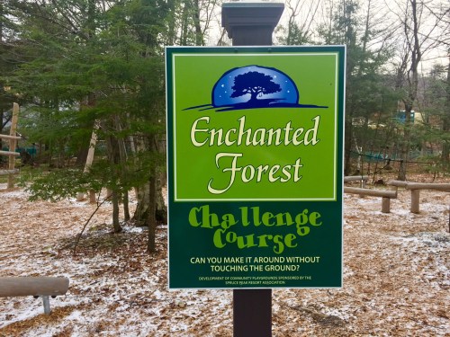 Sign for "Enchanted Forest Challenge Course" with a tree graphic, inviting visitors to navigate without touching the ground.