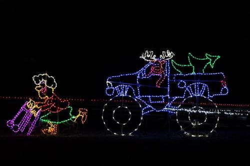 A colorful light display featuring a truck with reindeer antlers and a figure pulling a suitcase.