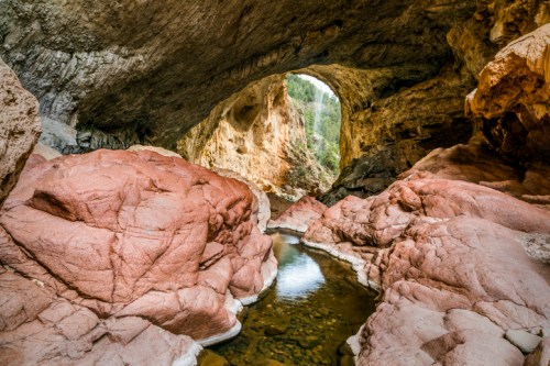 A scenic view of a rocky canyon with a river flowing beneath a large arching rock formation.