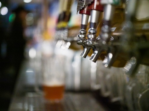 Close-up of beer taps with blurred background, showcasing a variety of draft options and a glass of beer.
