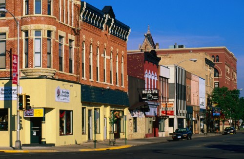 A vibrant street scene featuring historic brick buildings, shops, and clear blue skies.