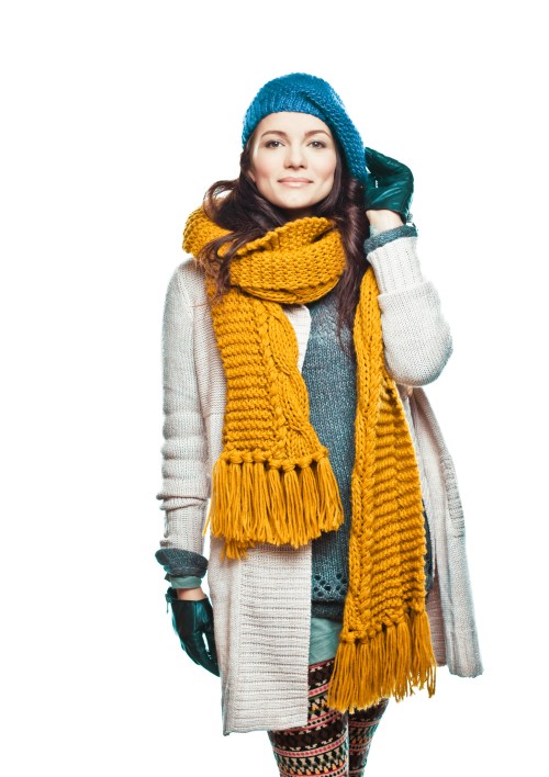 A woman in a blue beanie and yellow scarf smiles, wearing a cozy sweater and patterned leggings against a white background.
