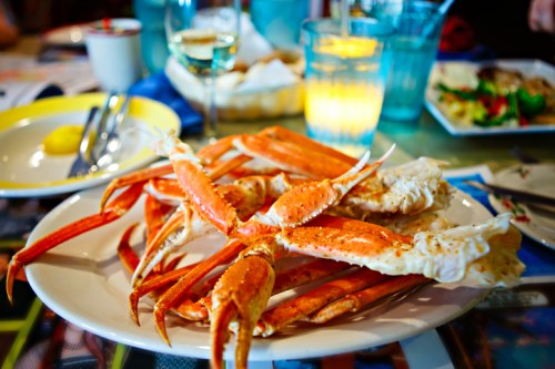 A plate of cooked crab legs surrounded by dining utensils and drinks on a table.