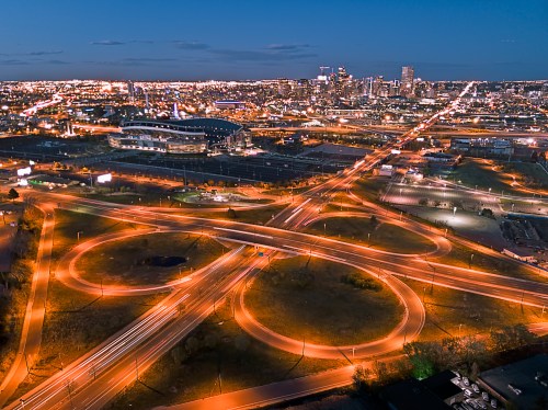 Aerial view of a city at dusk, featuring illuminated highways and a stadium, with a skyline in the background.