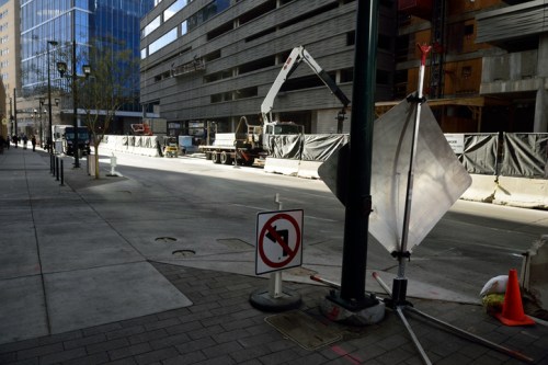 Construction site on a city street with barriers, a no left turn sign, and machinery in the background.